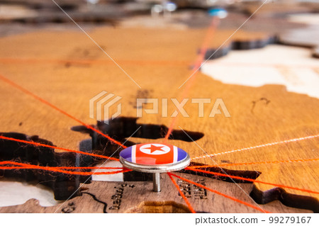 North Korea flag on the pushpin and red threads on the wooden map. Travel or logistic routes. Influence in geopolitics and world economy.  99279167