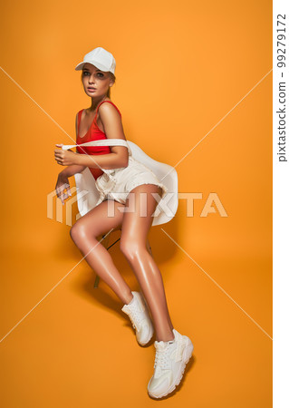 Full length of attractive girl in red swimsuit posing while sitting on chair on orange background 99279172
