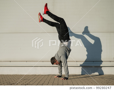 Caucasian man in hooded sweatshirt doing handstand outdoors. Caucasian man in hooded sweatshirt doing handstand outdoors. 99280247