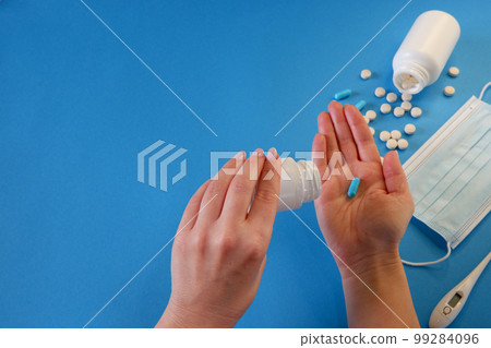 Medicine and healthcare concept. The woman removes the capsule from the container. Capsules, pills, medical mask on a blue background. Place for your text. Medicine and healthcare concept. The woman removes the capsule from the container. Capsules, pills, medical mask on a blue background. Place for your text. 99284096