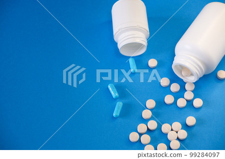 Medicine and healthcare concept. Capsules, tablets scattered near containers on a blue background. Place for your text. 99284097