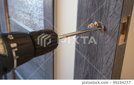 Insert of latch and handle into the interior door. Close-up view of the work process. Insert of latch and handle into the interior door. Close-up view of the work process. 99284257