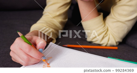 The girl makes a coloring with multi-colored pencils, close-up on hand. Home art hobby. The girl makes a coloring with multi-colored pencils, close-up on hand. Home art hobby. 99284369