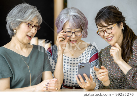 三名 50 多歲的女性正在看智能手機屏幕 99285276