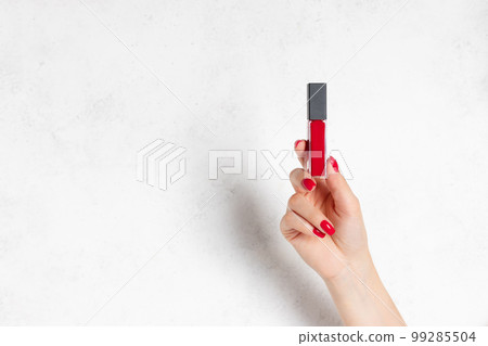 red liquid matte lipstick in female hand with red manicure. red liquid matte lipstick in female hand with red manicure. 99285504
