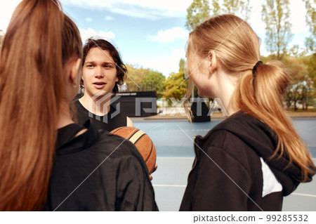 A company of young girls and boys is going to play basketball on the city playground. 99285532