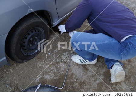 A man who is jacking up to replace a punctured car with a spare tire 99285681