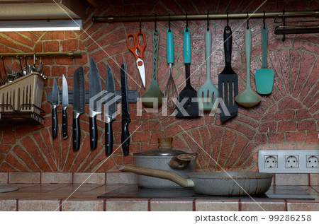 Brick-decorated kitchen wall with kitchen utensils hanging on it 99286258