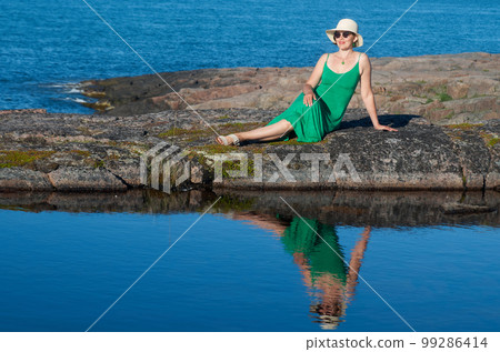 Woman tourist in a straw hat and a green dress on the seashore on a bright sunny day 99286414