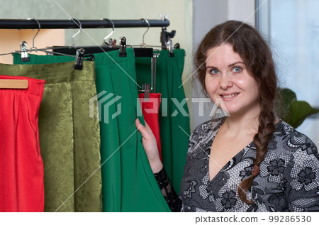 A clothing seller stands next to a rack with hangers A clothing seller stands next to a rack with hangers 99286530