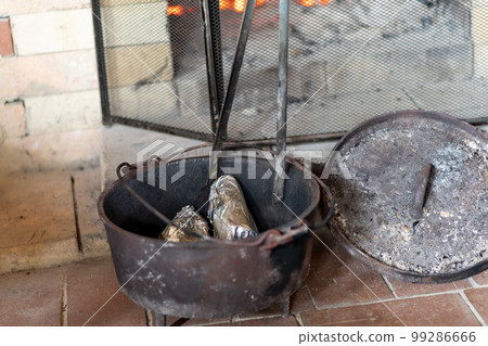 Roasting sweet potatoes in an old dutch oven in the fireplace of a mountain hut 99286666
