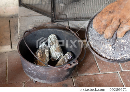 Roasting sweet potatoes in an old dutch oven in the fireplace of a mountain hut Roasting sweet potatoes in an old dutch oven in the fireplace of a mountain hut 99286671