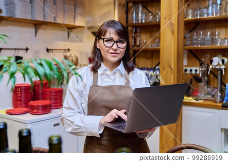 Portrait of middle aged woman working in restaurant holding laptop 99286919