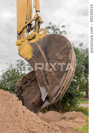 A bucket of excavator pours the ground into a heap against the background of a rural industrial zone. Bulldozer work on the construction site A bucket of excavator pours the ground into a heap against the background of a rural industrial zone. Bulldozer work on the construction site 99288019