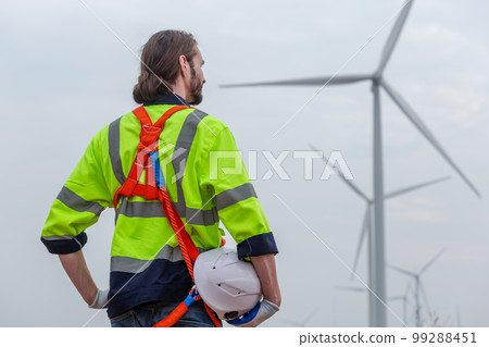 man engineer holding helmet safety wearing uniform standing at wind turbine. man engineer holding helmet safety wearing uniform standing at wind turbine. 99288451