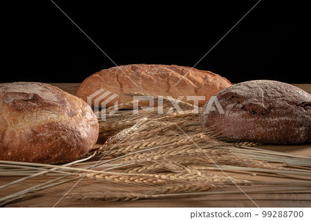 Three loaves of bread and ears of wheat on a black background 99288700