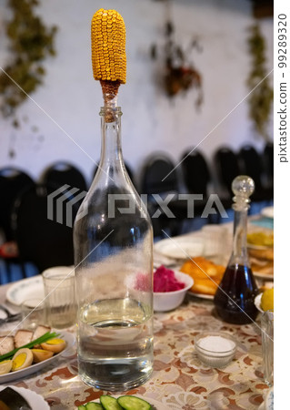 Big bottle of vodka with cob of corn as a stopper of a bottle, close-up. 99289320