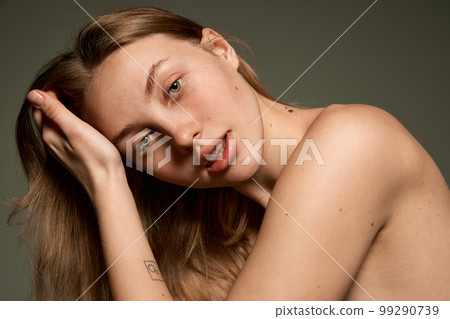 Closeup portrait of beautiful young girl with smooth clear skin and without makeup looking at camera with tenderness over grey background. Concept of natural beauty 99290739