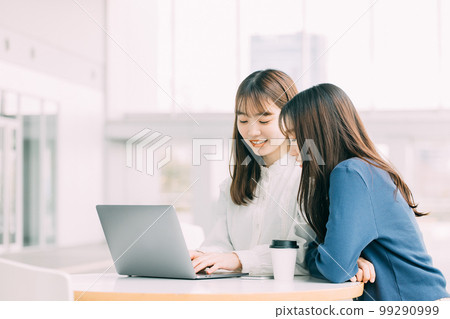 Two young Japanese businesswomen talking while using a laptop 99290999