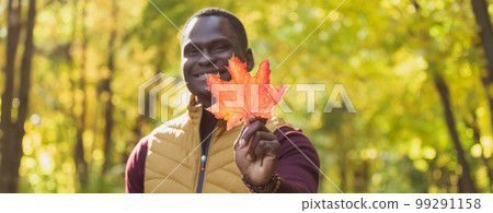 Banner close up portrait of african american man gives autumn maple leaf copy space. Autumn nature. Seasonal fall fashion. 99291158