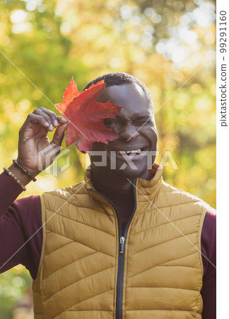Close up portrait of african american man covering his face with autumn maple leaf. Autumn nature. Seasonal fall fashion. 99291160