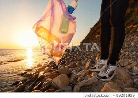 Coastal cleaning. Activist puts a picked-up plastic bottle in a garbage bag, close-up. The concept of cleanup from environmental pollution and Earth Day 99291929