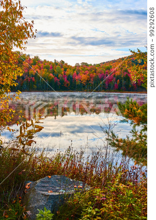 Peacefully foggy lake surface with peak foliage forests around 99292608