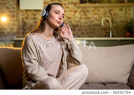 Purposeful young woman listening to music with headphones, dancing while sitting at home on the couch. Purposeful young woman listening to music with headphones, dancing while sitting at home on the couch. 99292784