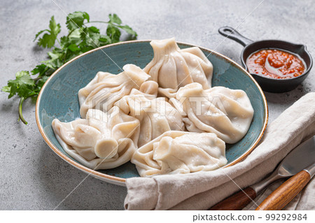 Georgian dumplings Khinkali on plate with red tomato sauce and fresh cilantro angle view, rustic stone background, traditional dish of Georgia Georgian dumplings Khinkali on plate with red tomato sauce and fresh cilantro angle view, rustic stone background, traditional dish of Georgia 99292984