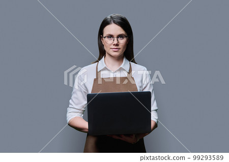 Young woman in apron using laptop on grey studio background Young woman in apron using laptop on grey studio background 99293589