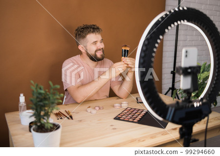 Man recording video vlog while applying cosmetics or explore cosmetic product. Guy making tutorial make-up for his blog on cosmetics. Man recording video vlog while applying cosmetics or explore cosmetic product. Guy making tutorial make-up for his blog on cosmetics. 99294660