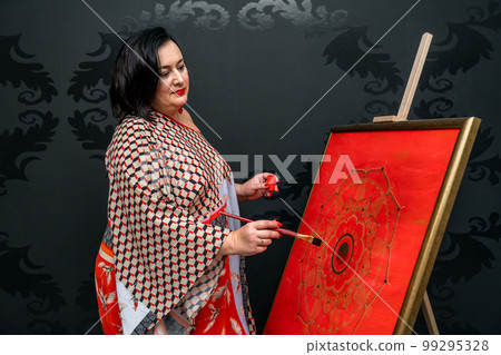 the artist draws a mandala with a brush and red paint on the canvas 99295328