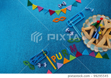 Purim celebration concept. Jewish carnival background. hamantaschen or hamans ears cookies, carnival mask and noisemaker Purim celebration concept. Jewish carnival background. hamantaschen or hamans ears cookies, carnival mask and noisemaker 99295545