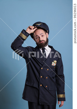 Airplane capitan taking hat off, looking at camera with confused facial expression. Puzzled aviation academy plane pilot front view, navy aviator holding cap with airforce badge wings Airplane capitan taking hat off, looking at camera with confused facial expression. Puzzled aviation academy plane pilot front view, navy aviator holding cap with airforce badge wings 99296013