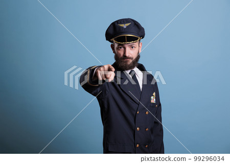 Serious airplane pilot pointing at camera, plane captain wearing uniform and hat front view portrait. Aviation academy aviator with airline wings badge on jacket looking at you Serious airplane pilot pointing at camera, plane captain wearing uniform and hat front view portrait. Aviation academy aviator with airline wings badge on jacket looking at you 99296034
