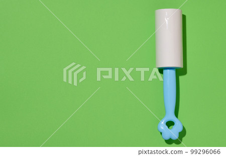 Roller with sticky tape for cleaning clothes on a green background, top view 99296066