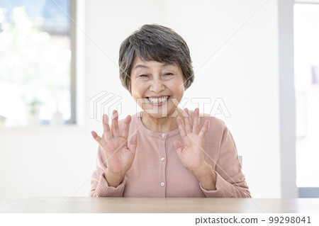 Portrait of a smiling elderly woman waving her hands looking at the camera 99298041