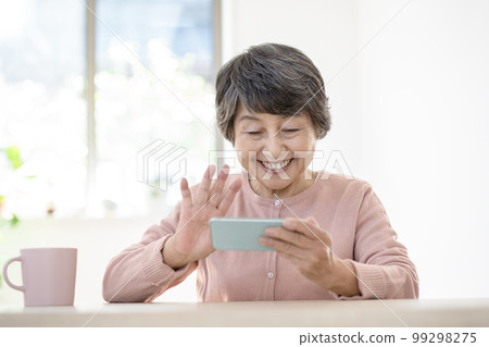 Elderly woman waving at smartphone Elderly woman waving at smartphone 99298275