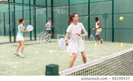 Woman playing padel. In the background, athletes are training 99299437