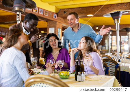 Men chatting with group of women in restaurant 99299447
