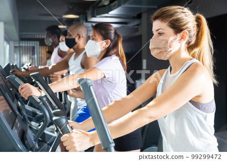 Active people in protective masks having running elliptical trainer class in club Active people in protective masks having running elliptical trainer class in club 99299472