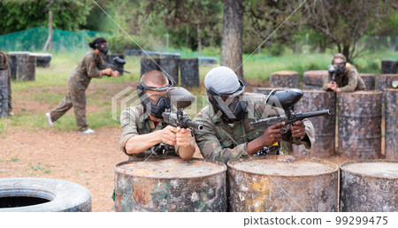 Two paintball player in camouflage and mask aiming with gun in shootout Two paintball player in camouflage and mask aiming with gun in shootout 99299475