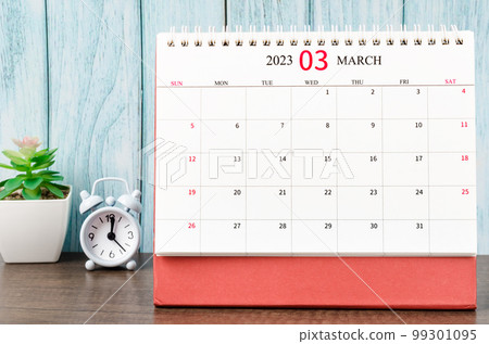 The March 2023 Monthly desk calendar for the organizer to plan 2023 year with alarm clock on wooden table. 99301095