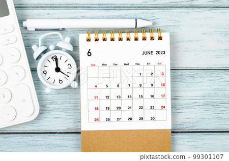 The June 2023 Monthly desk calendar for the organizer to plan 2023 year with alarm clock and calculator on wooden table. 99301107