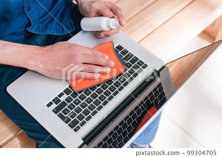 top view. a young man treating the laptop from bacteria coronavirus top view. a young man treating the laptop from bacteria coronavirus 99304705