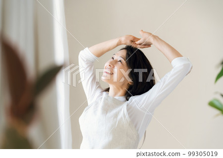 A middle-aged woman bathing in the sunlight by the window 99305019