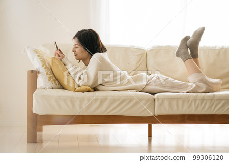 Woman watching smartphone on sofa 99306120