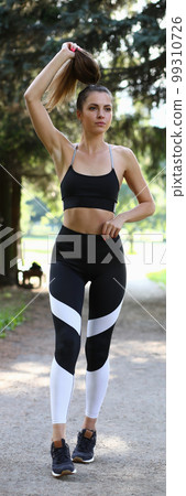 Young beautiful woman dressed in sportswear poses against backdrop of forest park 99310726