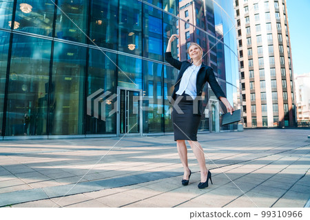 Happy business woman showing thumbs up while standing outdoors against office Happy business woman showing thumbs up while standing outdoors against office 99310966