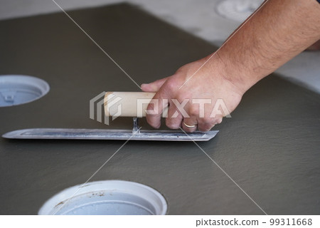 A craftsman holding down concrete with a trowel at a construction site A craftsman holding down concrete with a trowel at a construction site 99311668